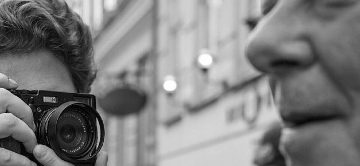 Fotógrafo captando de cerca el rostro de un hombre en una escena urbana en blanco y negro