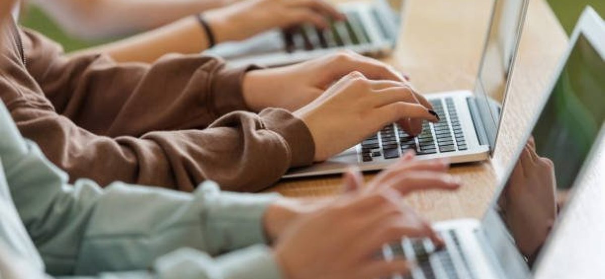 High school students sitting at the desk in the classroom during lesson, using laptops. Close up of hands, unrecognizable people.