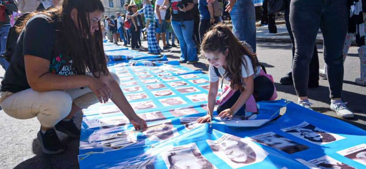 Nena sobre bandera con nombres de desaparecidos durante la marcha del 24 de marzo en La Plata